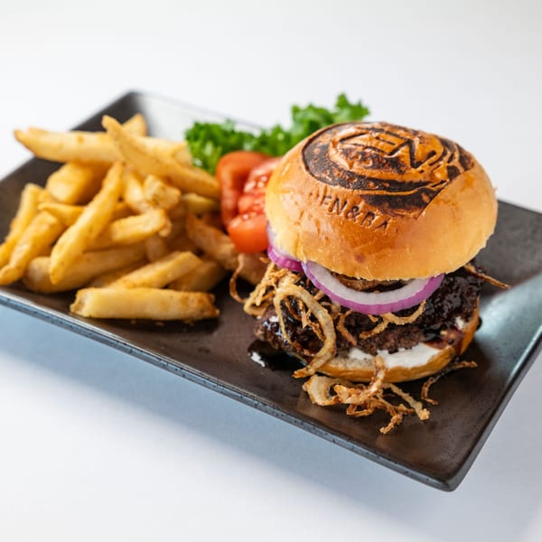 ZEN Kitchen & Bar's branded burger with fries, lettuce, tomato, and onion on a dark plate.