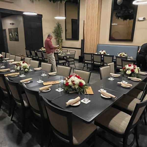 A long, dark U-shaped dining table set with floral centerpieces, glasses, and rolled napkins at ZEN Kitchen & Bar.